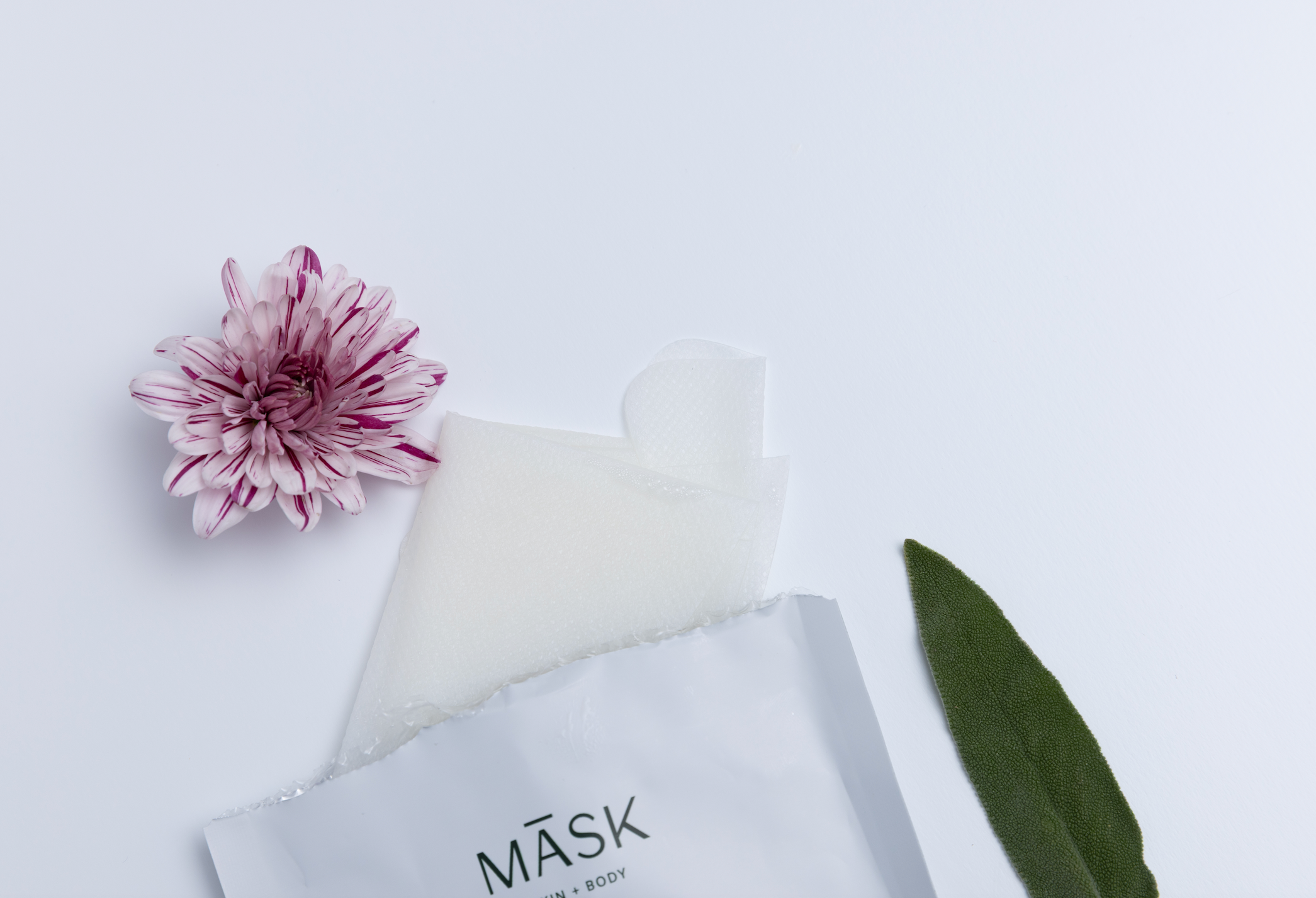Minimalist flatlay of MĀSK Skincare sheet mask with soft botanical elements, representing a clean and simple skinimalism routine.